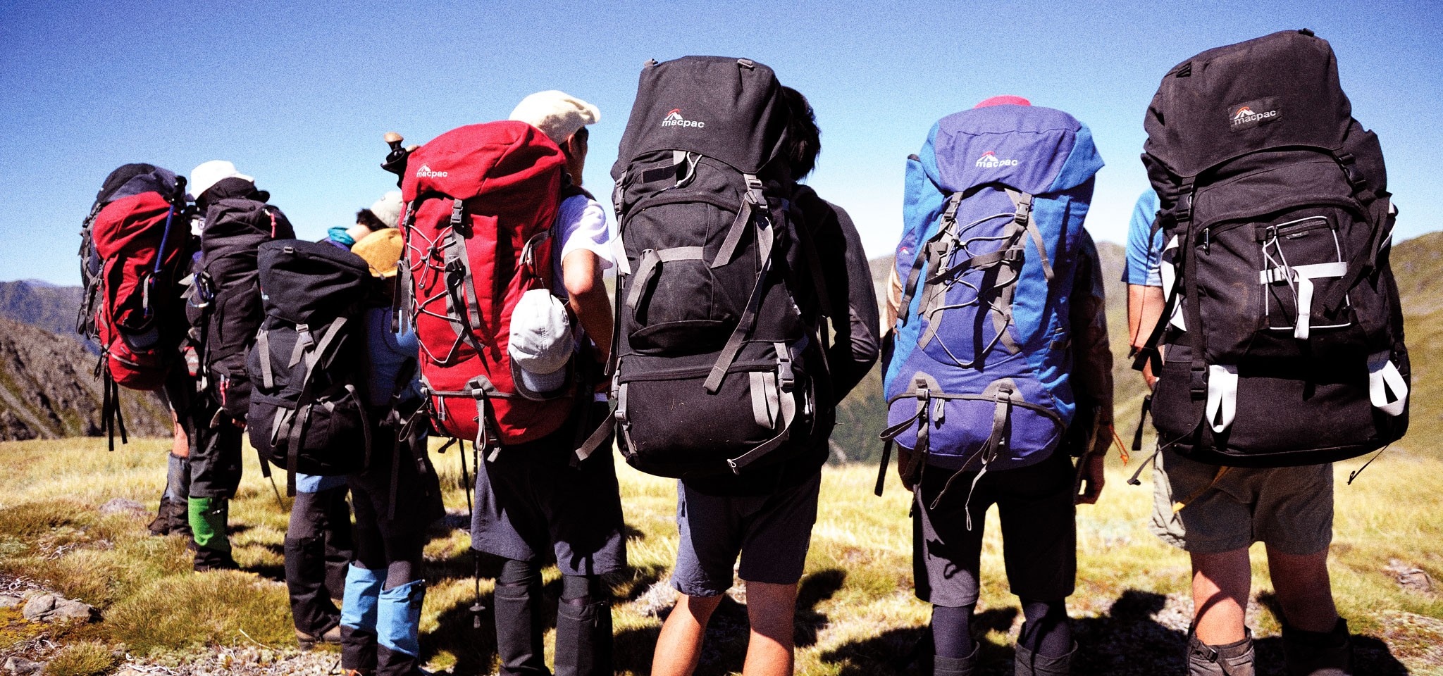 People standing wearing Macpac tramping packs outside on a sunny day