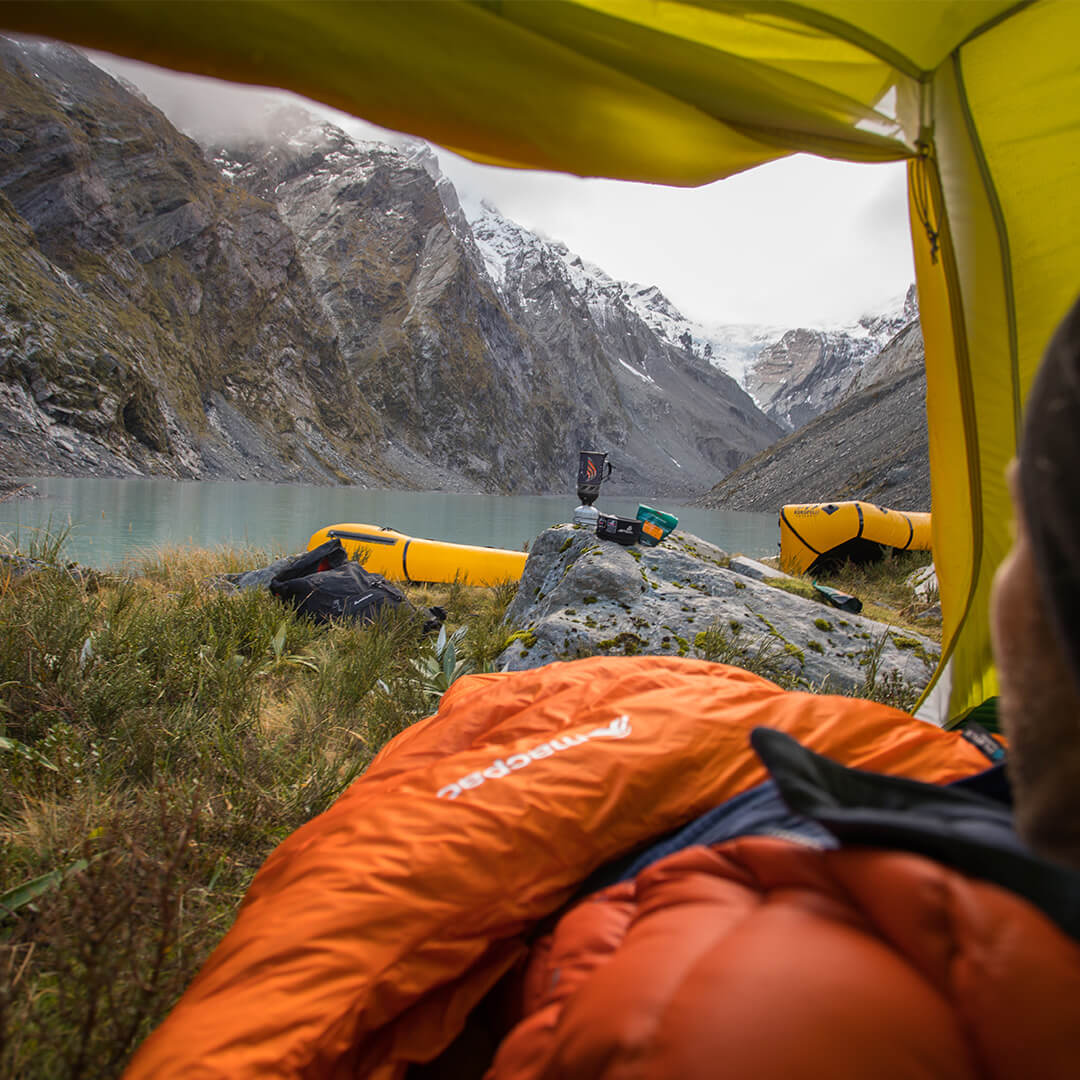 Person looking out of tent overlooking mountain lake