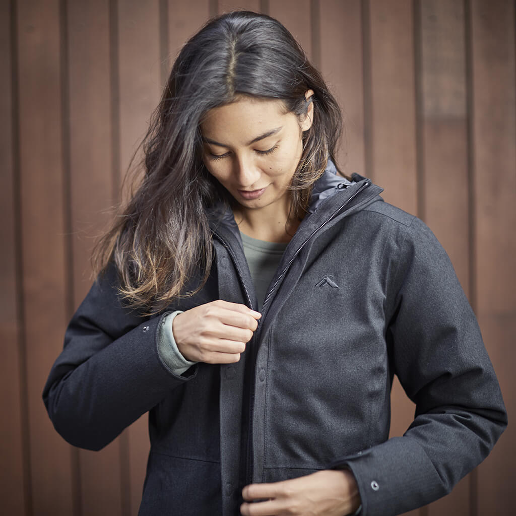 Woman zipping up a black element jacket in front of a timber wall