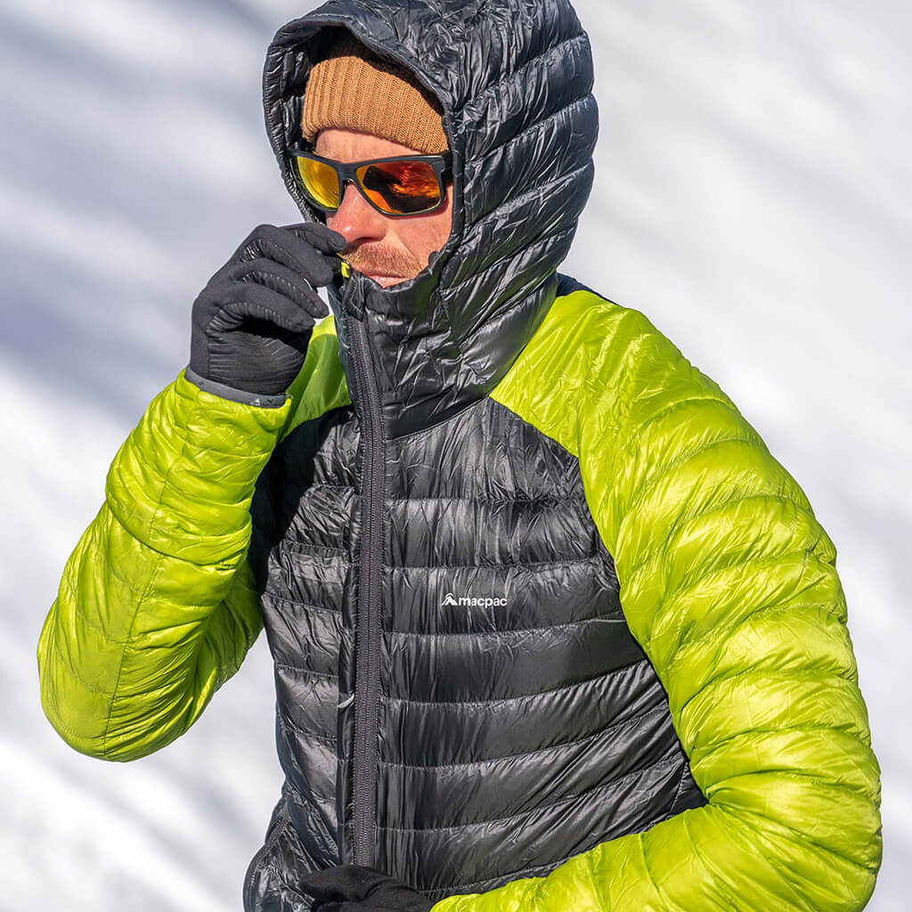 A man zipping up a grey and green Icefall jacket with a white snow background