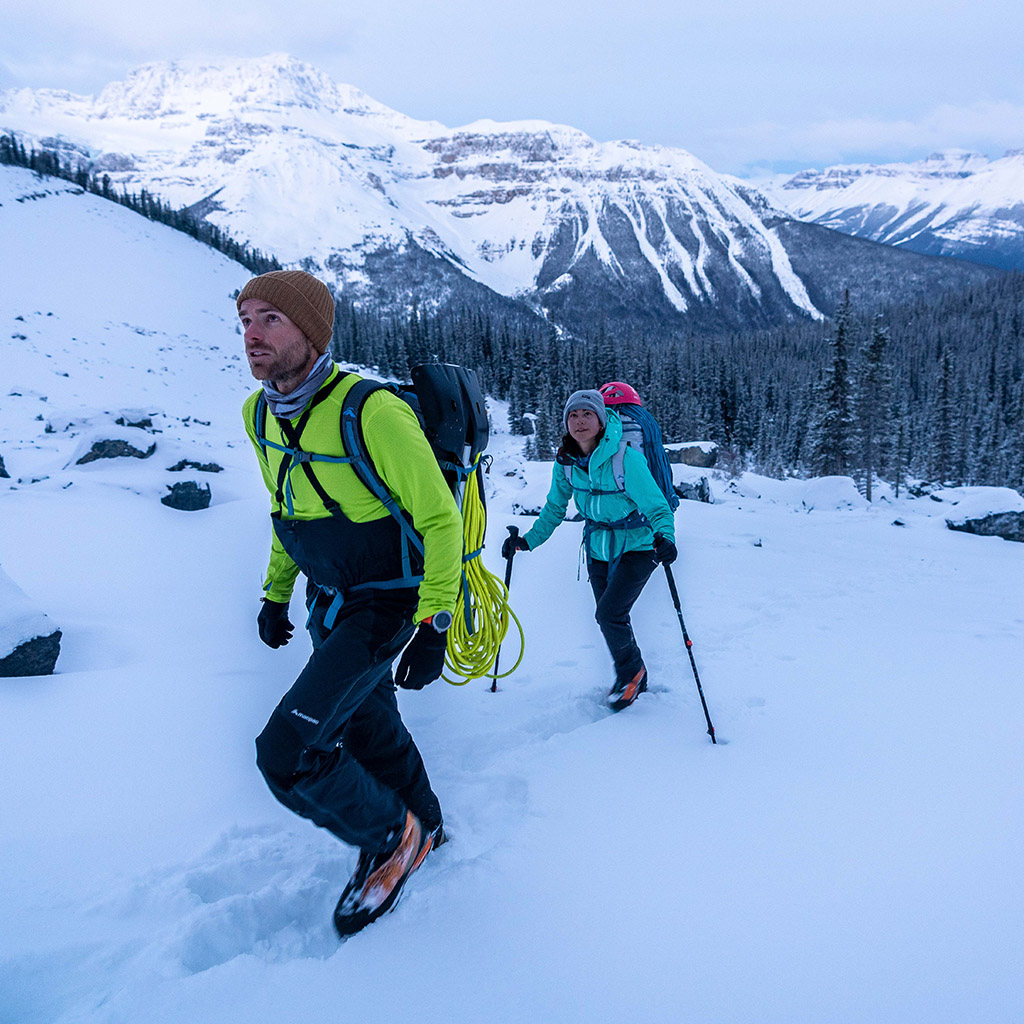 2 NZ alpine team members hiking through snow in yellow and blue jacket