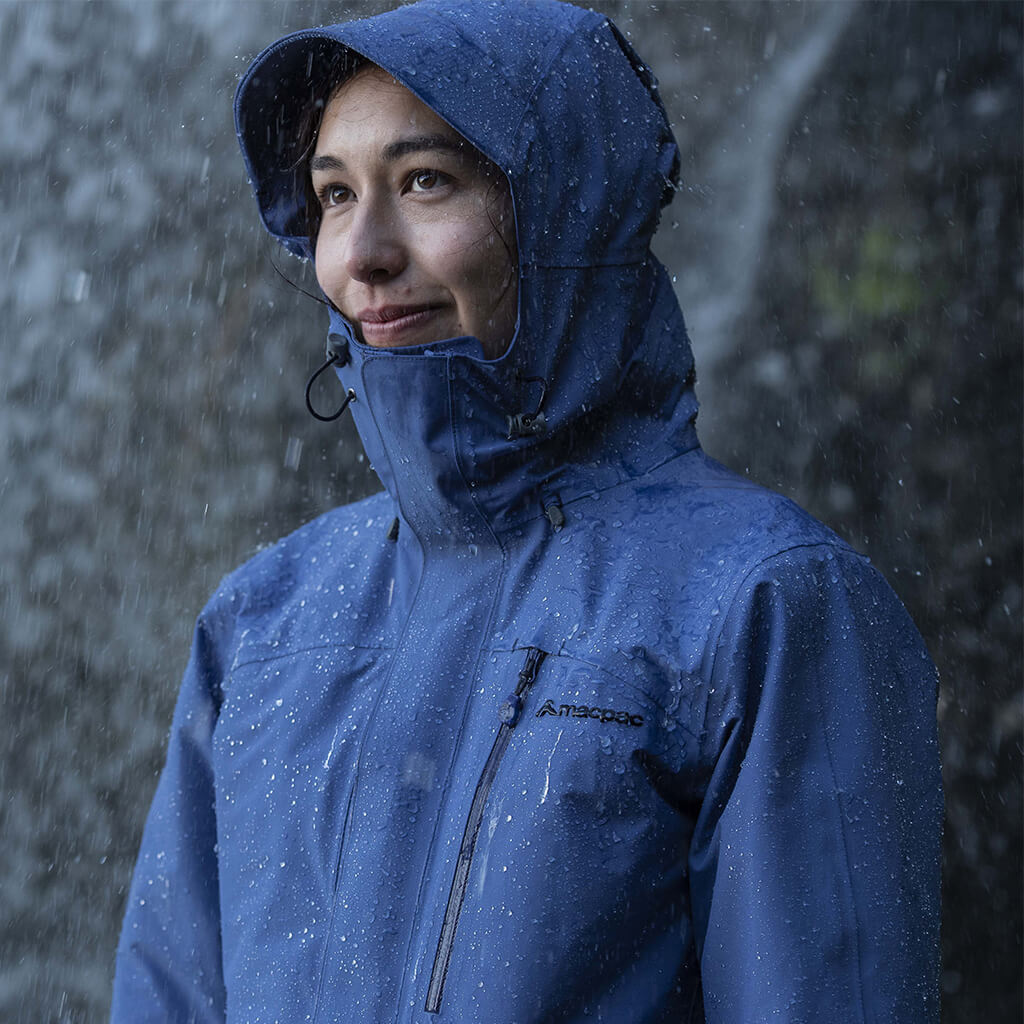 A woman wearing a blue macpac rain jacket with hood up in heavy rain 