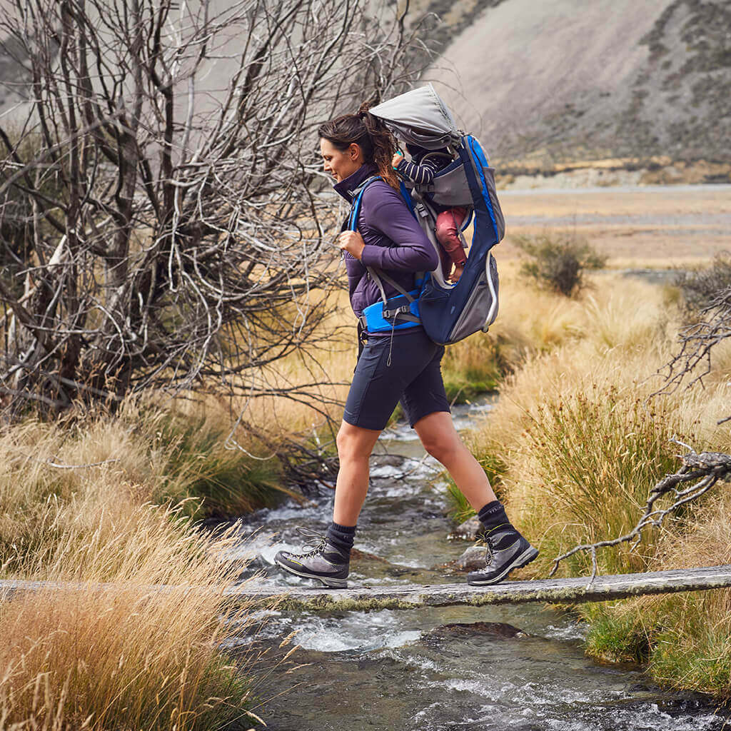 Woman walking over creek wearing a hiking pack and boots