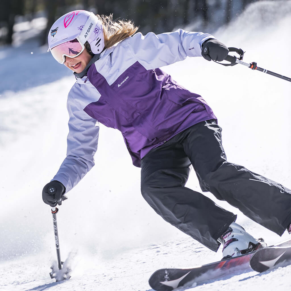 Woman wearing a pink and black powder jacket with ski helment and goggles standing on snow