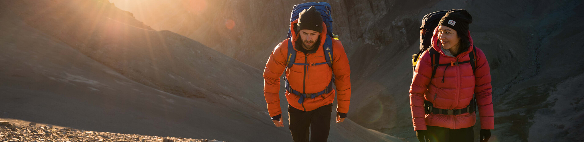 2 people hiking up a mountain wearing brightly coloured puffer jackets