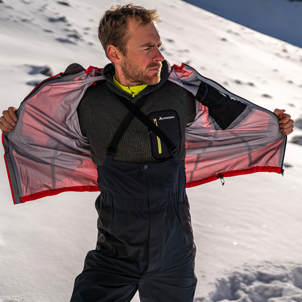 man pealing off red jacket showing bib pants and mid layers