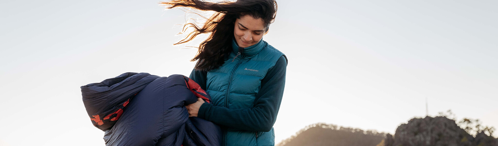 Woman holding navy blue sleeping bag, standing outside in breeze