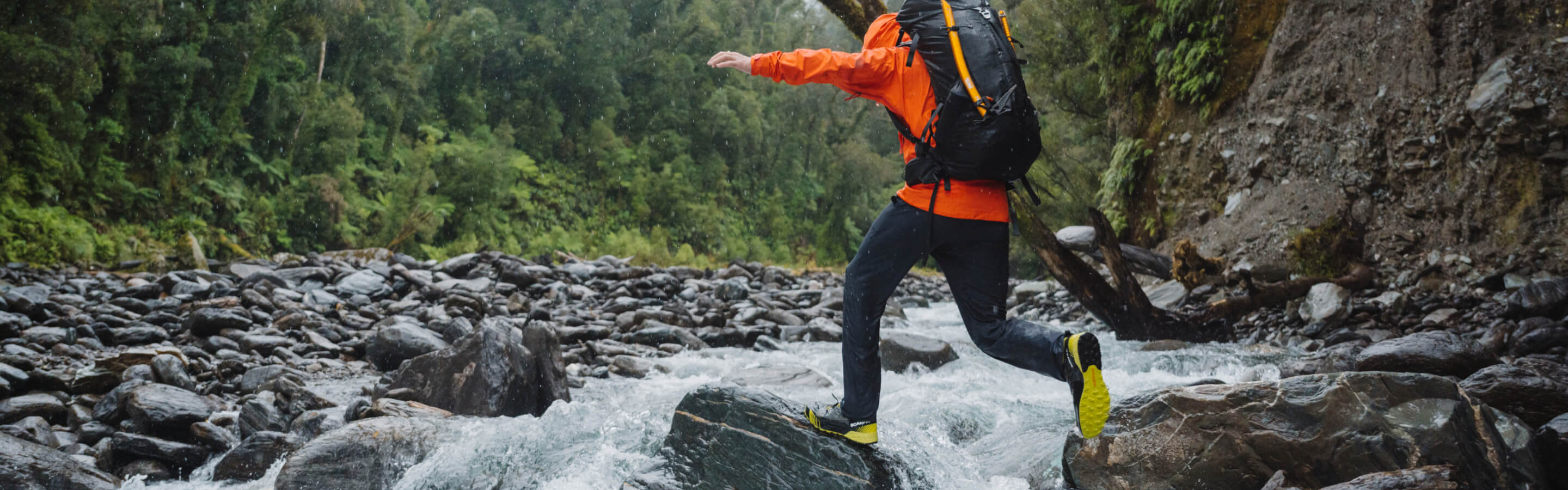 Person in orange rain jacket crossing rugged river