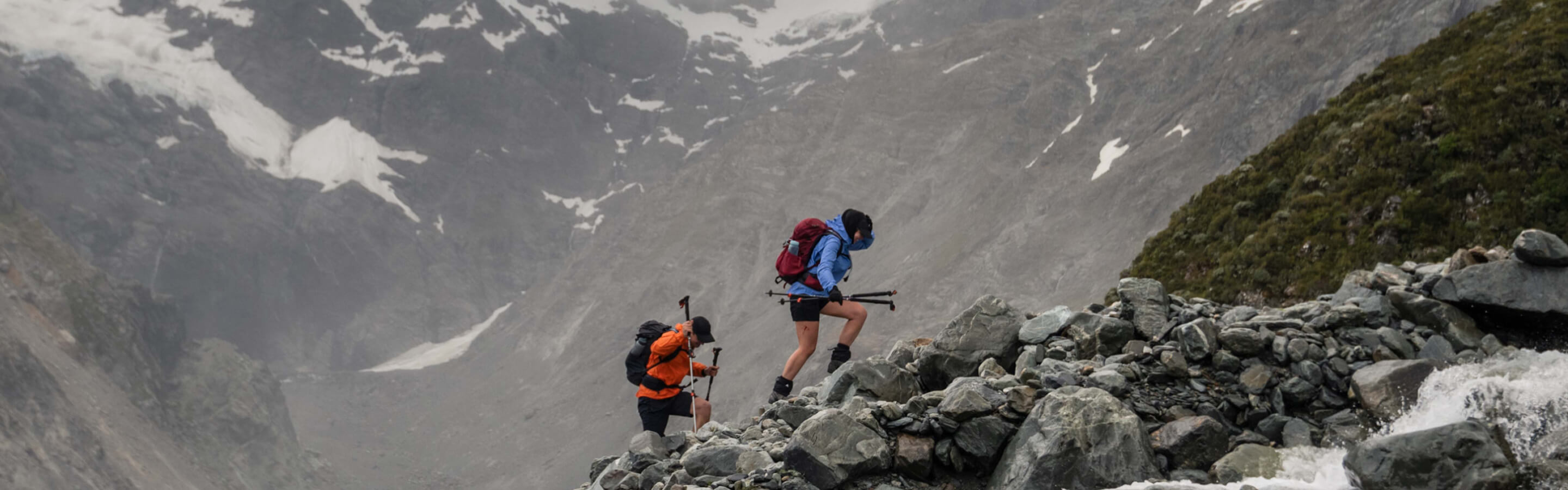 Person in orange rain jacket crossing rugged river