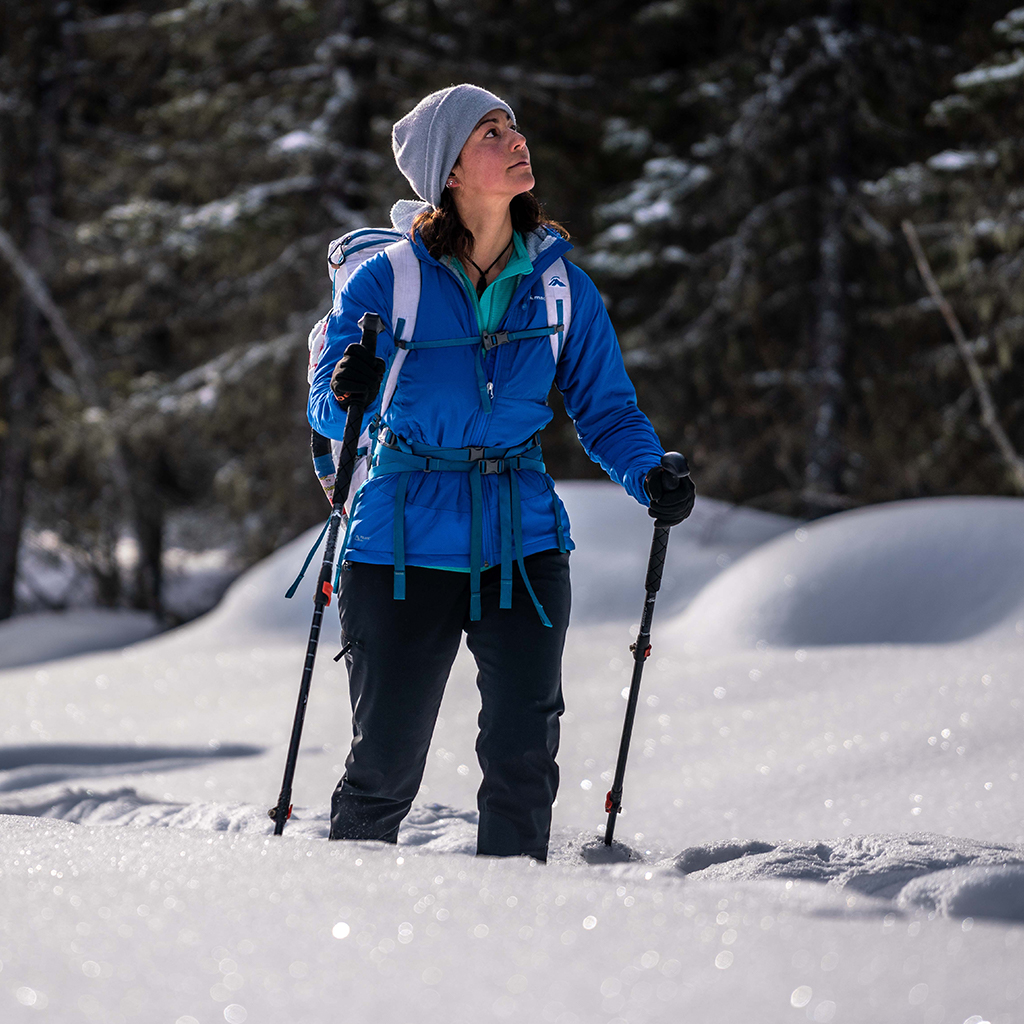 Woman wearing Blue jacket walking through snow using hiking poles