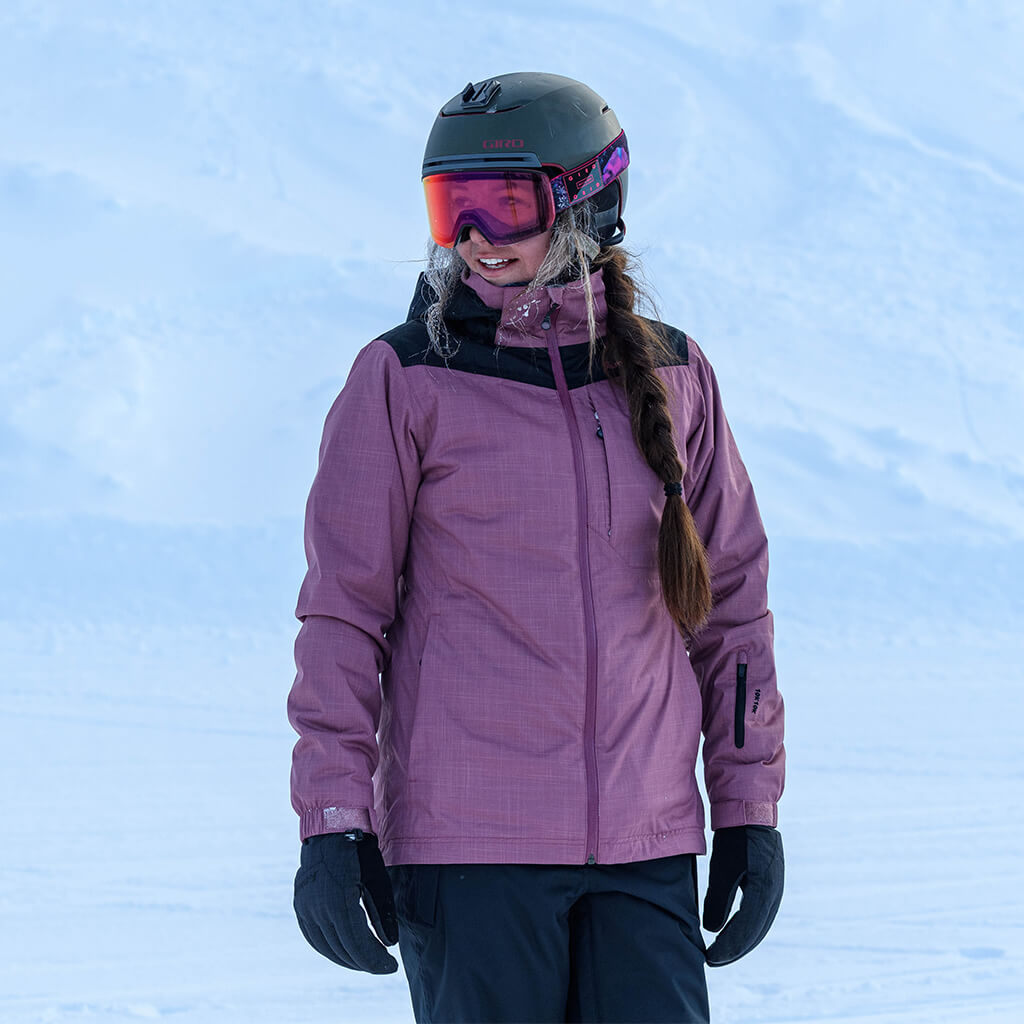 Woman wearing a pink and black powder jacket with ski helment and goggles standing on snow