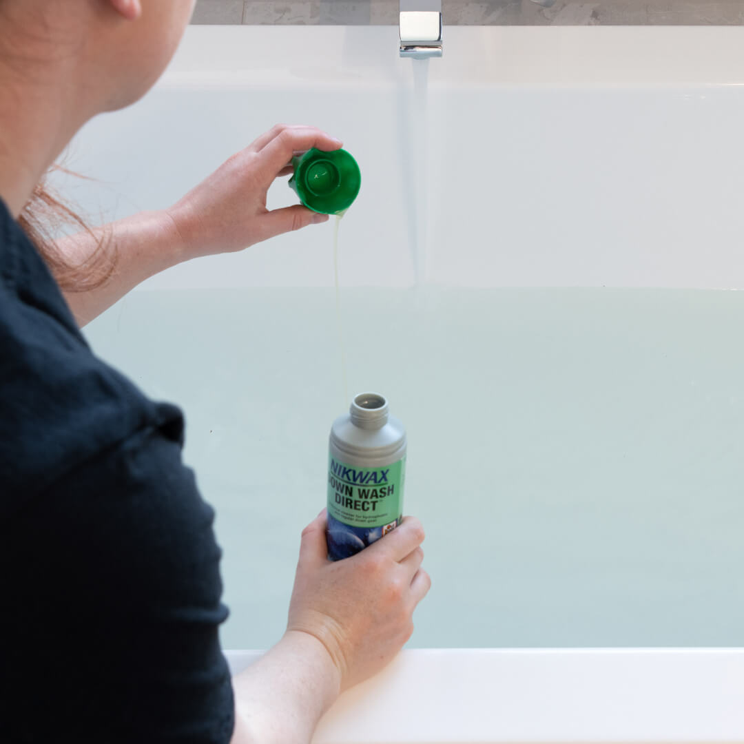 Person adding a capful of Nikwax Down Wash Direct to a tub of water