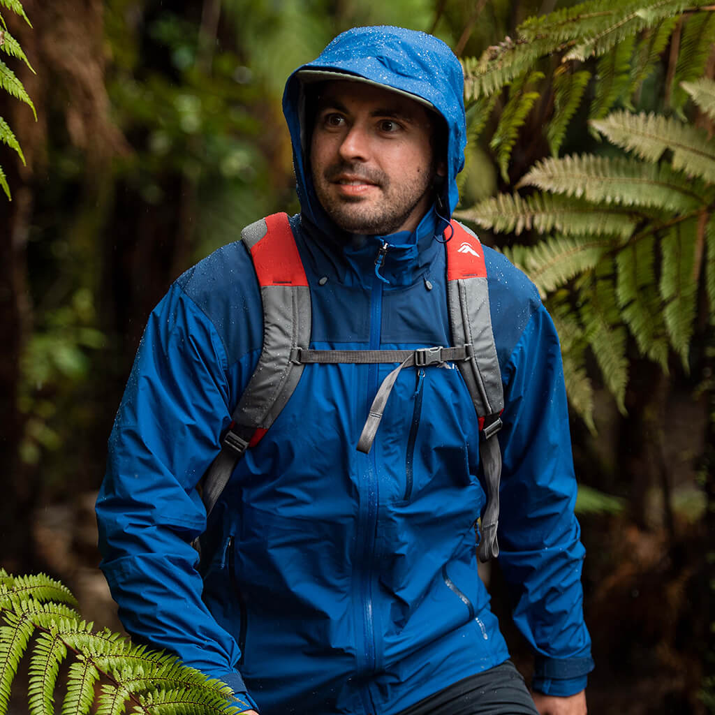 A man and a woman wearing hooded rain jackets hiking through a river using poles