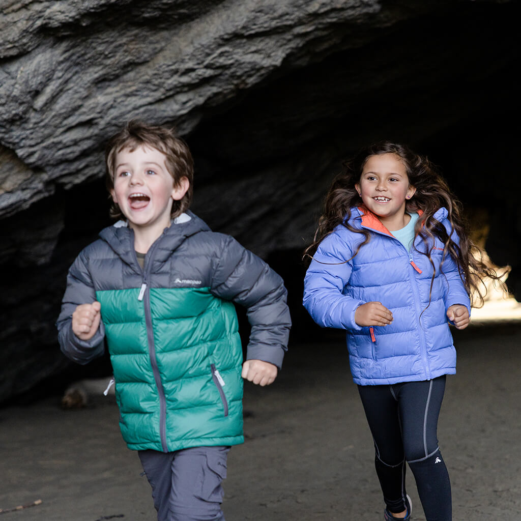 2 children wearing brightly coloured down jackets running through a rocky cave