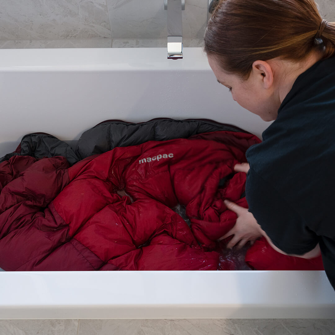 Person washing a red macpac sleeping bag in a bath