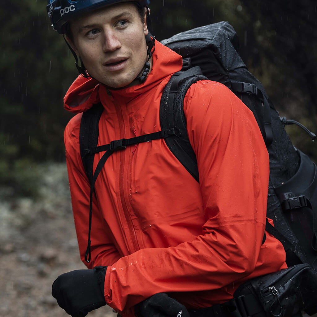 Man wearing orange rain jacket with a bike helmet on